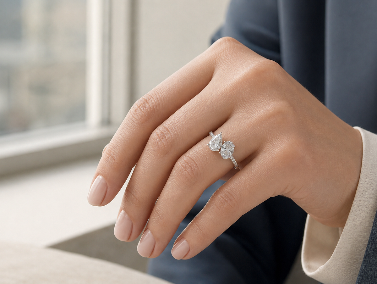 Hand wearing a Toi et Moi engagement ring with pear and oval diamond stones in soft window light.