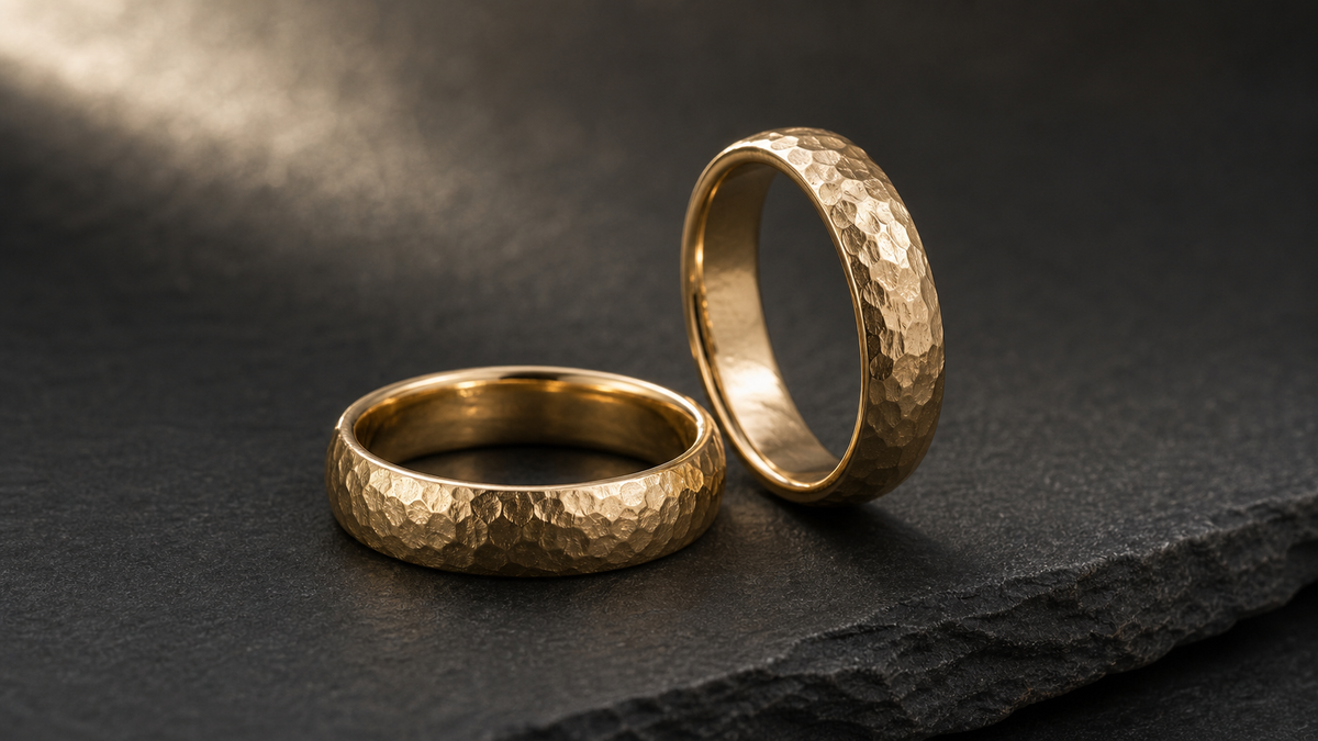 Pair of hammered wedding bands with faceted metal texture under angled studio light.