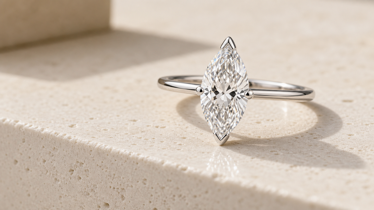 Marquise diamond engagement ring with V-prongs on a warm ivory stone step.