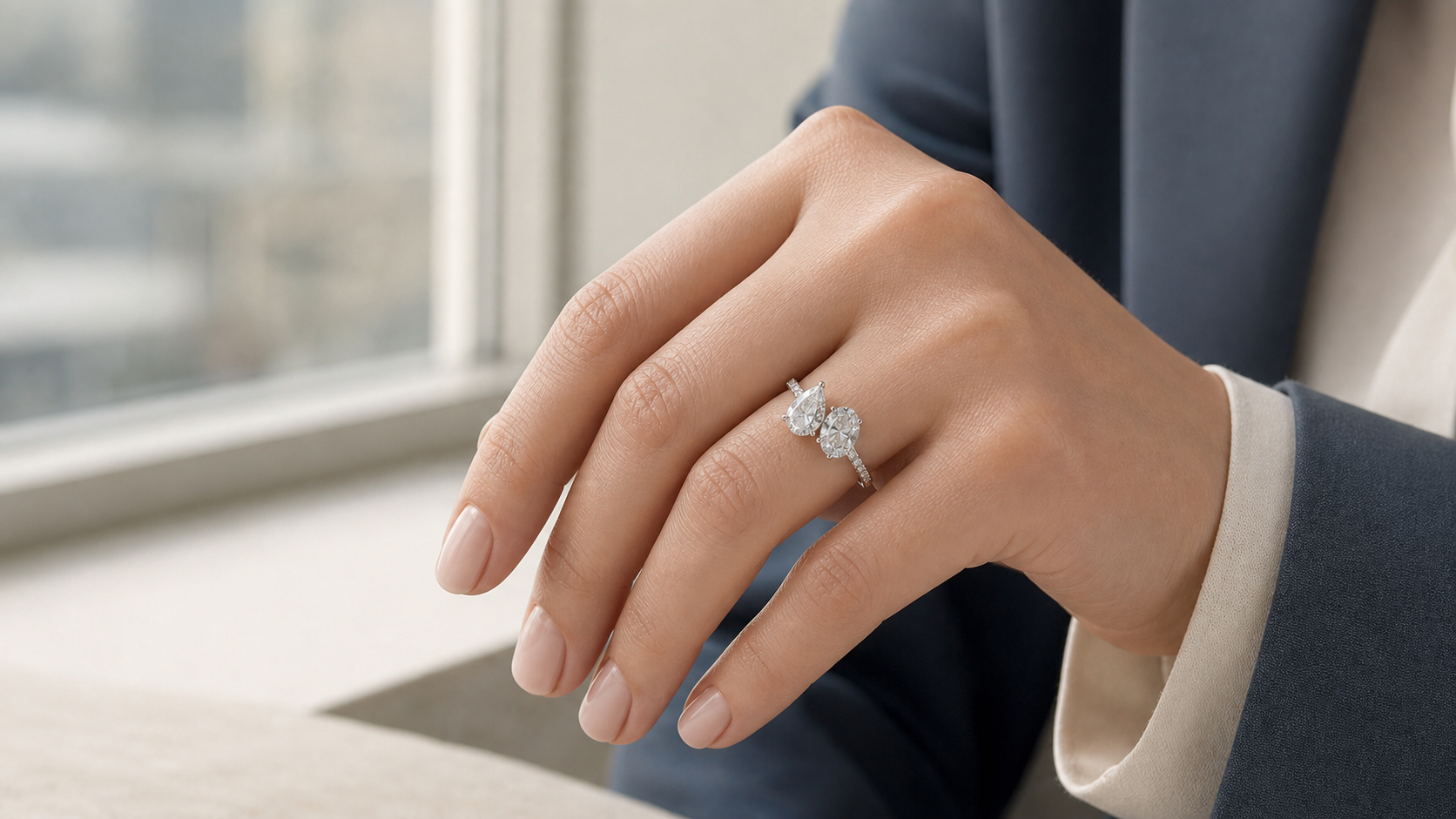 Hand wearing a Toi et Moi engagement ring with pear and oval diamond stones in soft window light.